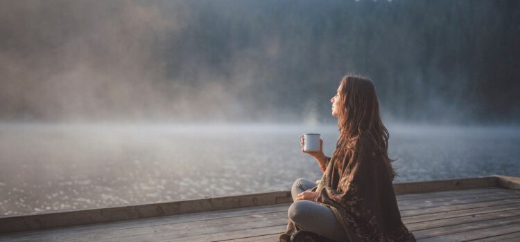 Woman sitting by lake with coffee in hand